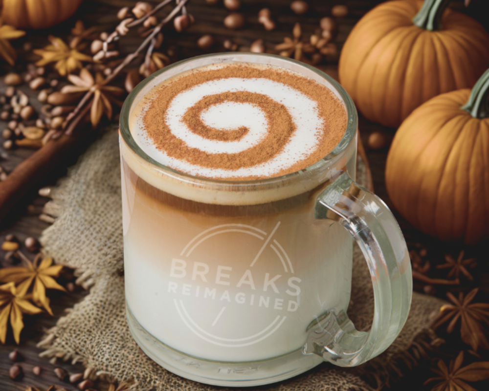 Coffee beverage with swirled cream design in glass mug with pumpkins & cloves in the background.
