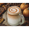 Coffee beverage with swirled cream design in glass mug with pumpkins & cloves in the background.