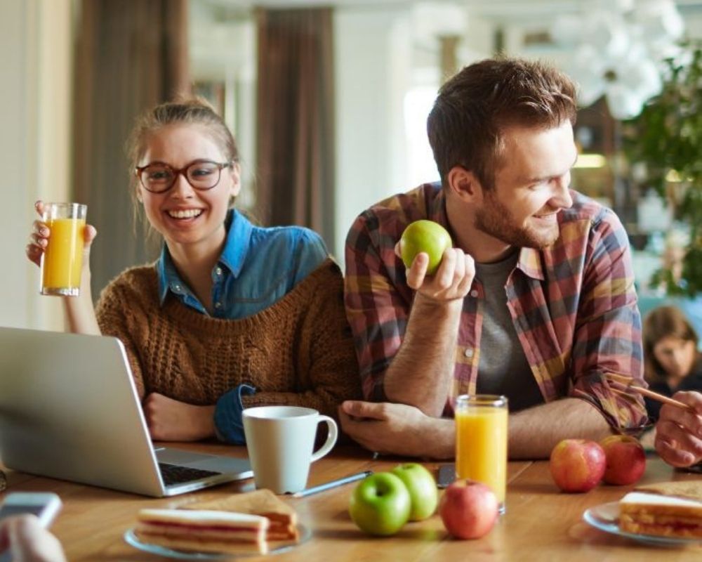 Coworkers enjoying a casual office break with healthy snacks and drinks, including apples, juice, and coffee, gathered around a table.