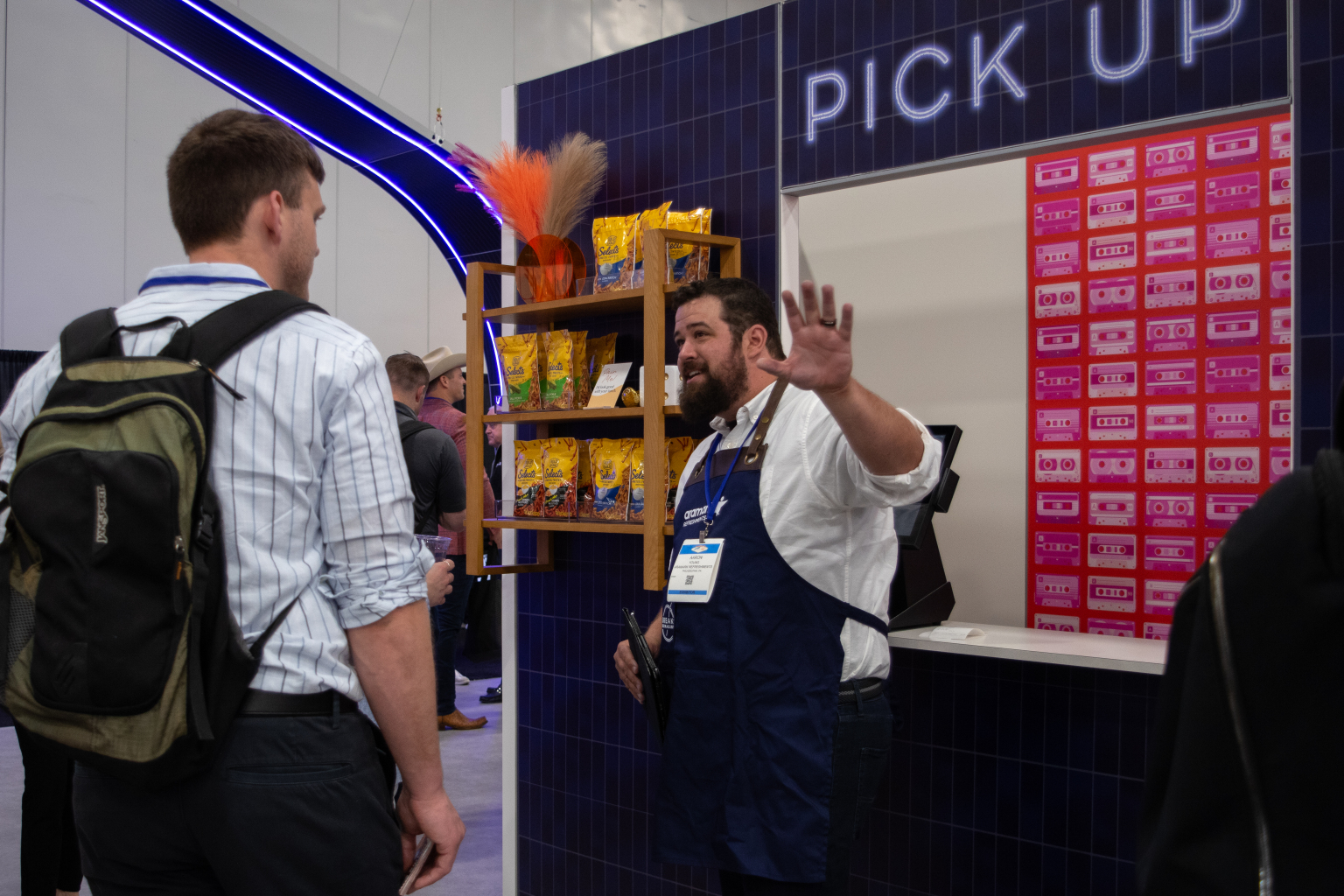 Aramark Refreshments employee standing in front of a pick-up window engaging with visitors with a snack display to the left