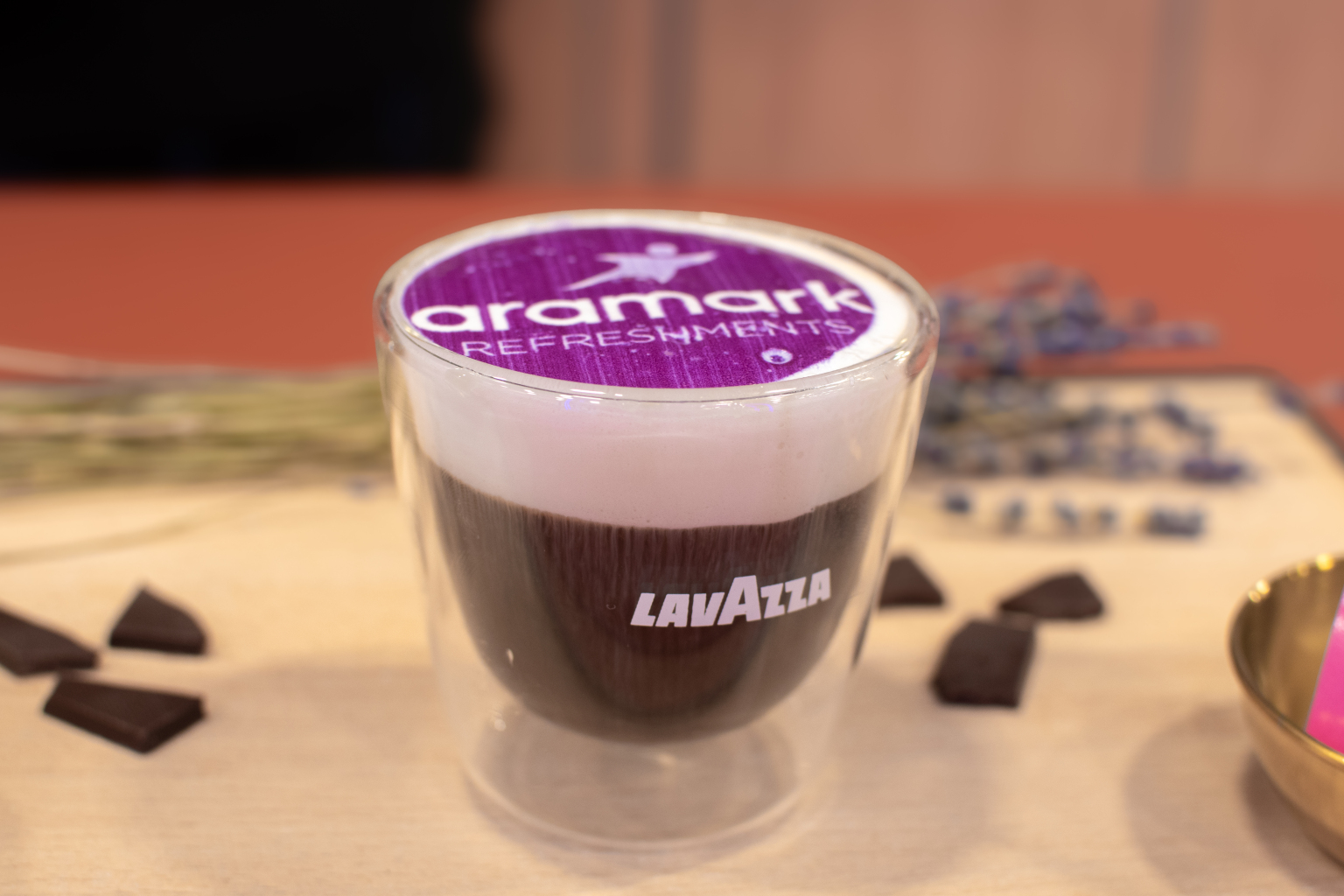 Glass cup of Lavazza chocolate coffee dessert topped with foam and a purple Aramark Refreshments logo